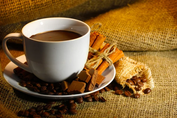 Xícara de café e feijão, paus de canela e chocolate no fundo de saque — Fotografia de Stock