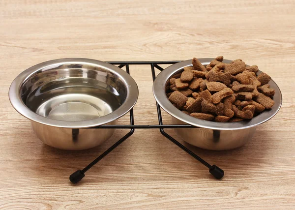 Suchý pes potravin a vody v kovové misky na dřevěné pozadí — Stock fotografie