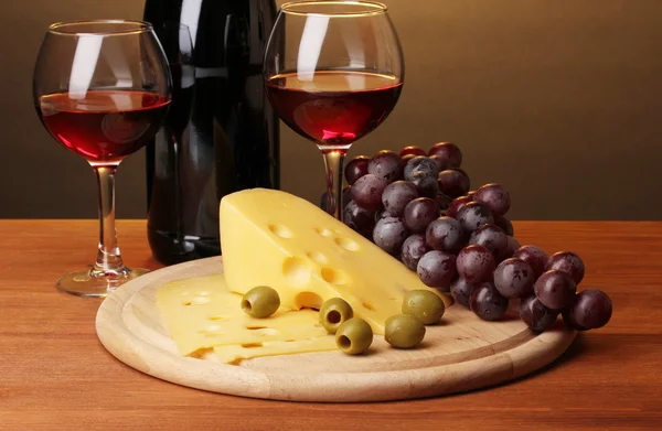 Láhev značkového vína s pohárky a sýrem na dřevěný stůl na hnědé pozadí — Stock fotografie