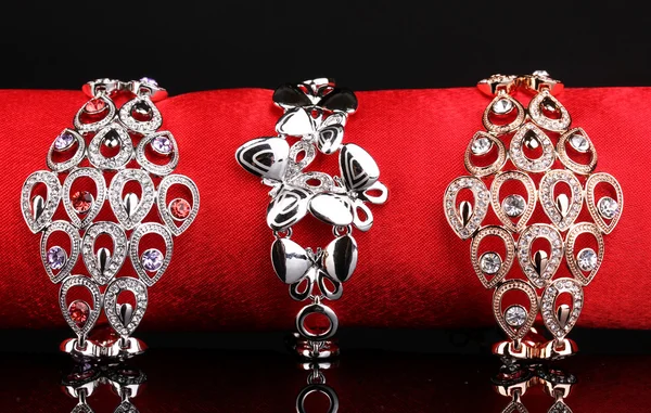 Três pulseiras elegantes no pano vermelho no fundo preto — Fotografia de Stock