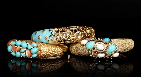 Красивые золотые браслеты с голубыми драгоценными камнями изолированы на черном фоне — стоковое фото