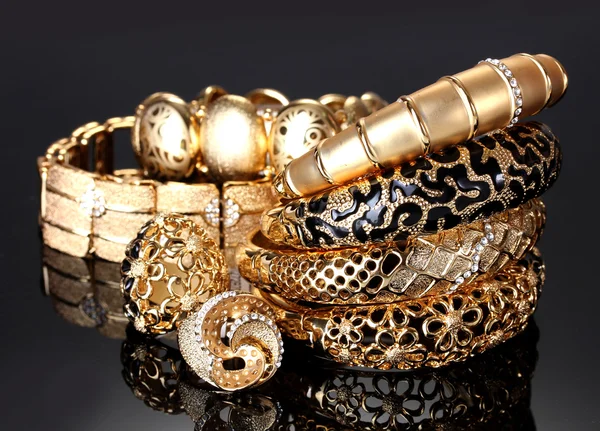 Schöne goldene Armbänder und Ringe auf grauem Hintergrund — Stockfoto