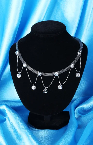 Красивое серебряное ожерелье на манекене на голубой шелковой ткани — стоковое фото