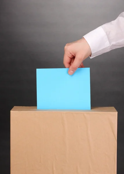 Mano con scheda elettorale e scatola su sfondo grigio — Foto Stock
