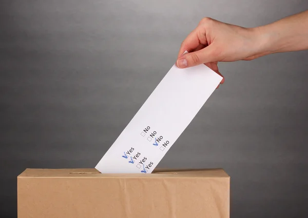 Mão com cédula de voto e caixa em fundo cinza — Fotografia de Stock