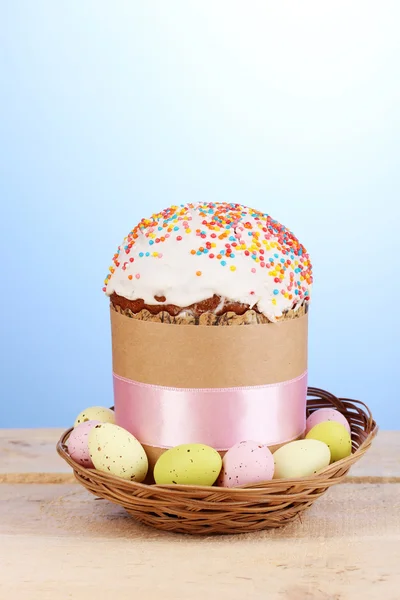 Vackra påsk kaka i korg med ägg på träbord på blå bakgrund — Stockfoto