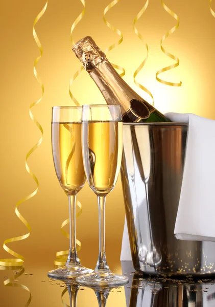 Champagneflaska i hink med is och glas champagne, på gul bakgrund — Stockfoto