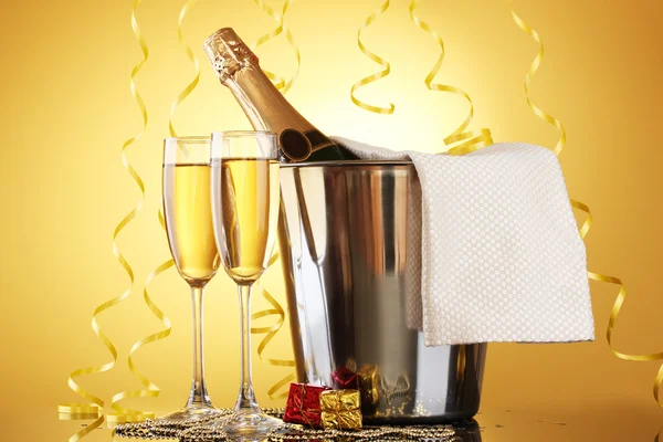 Bottiglia di champagne in secchio con ghiaccio e bicchieri di champagne, su fondo giallo — Foto Stock