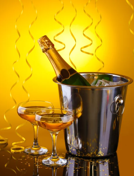 Üveg pezsgő vödörben jég és a pohár pezsgő, sárga háttér — Stock Fotó