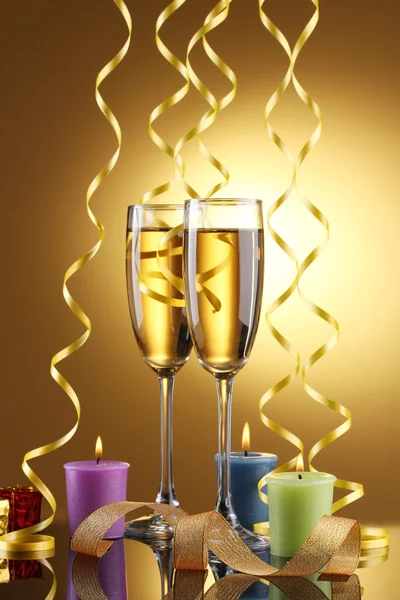 Glasses of champagne, candles, gifts and streamer on yellow background — Stock Photo, Image