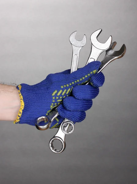 Wrenches in hand with protection glove on grey background — Stock Photo, Image