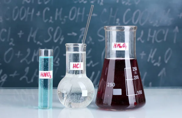 Tubos de ensaio com vários ácidos e outros produtos químicos no fundo do quadro negro — Fotografia de Stock