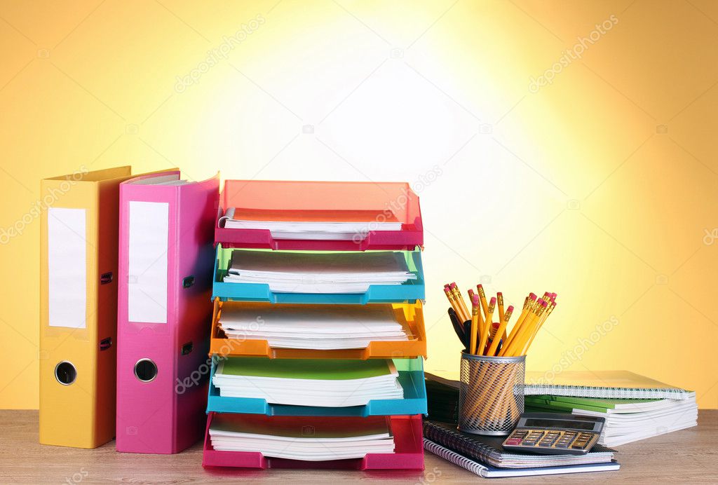 Bright paper trays and stationery on wooden table on yellow background