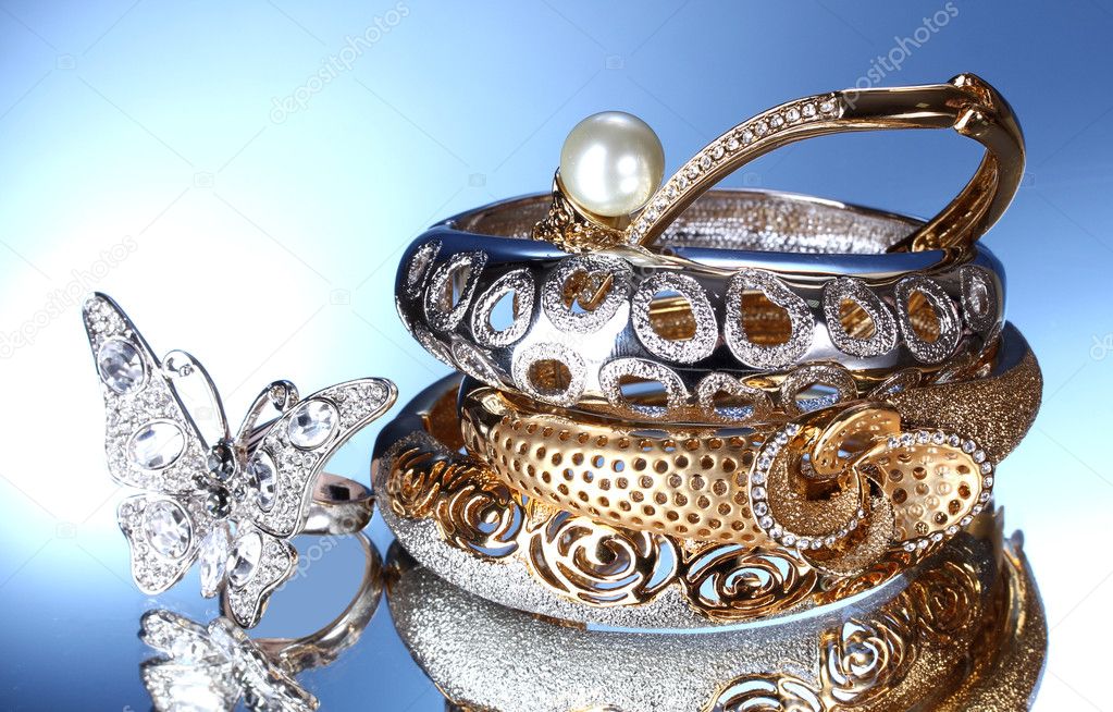 Beautiful silver and gold bracelets and ring on blue background