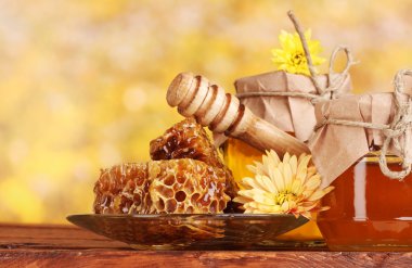 Two jars of honey,honeycombs and wooden drizzler on table on yellow background clipart