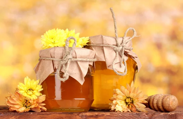 Due vasetti di miele e drizzler in legno su tavola su fondo giallo — Foto Stock