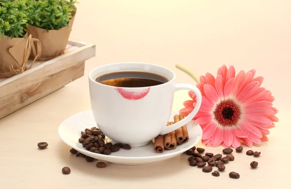 Cup of coffee with lipstick mark and gerbera beans, cinnamon sticks on wooden table — Stock Photo, Image