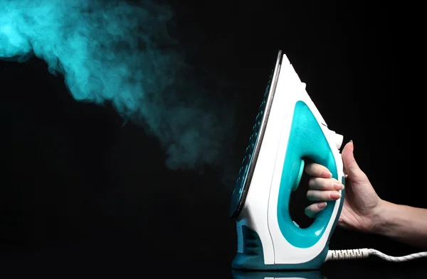 Electric iron with blue steam on black — Stock Photo, Image