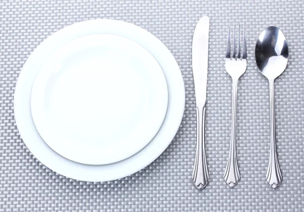 Белые пустые тарелки с вилкой, ложкой и ножом на серой скатерти — стоковое фото