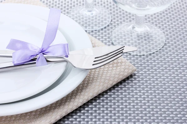 Assiettes blanches vides, fourchette et couteau attachés avec un ruban et des lunettes sur une nappe grise — Photo