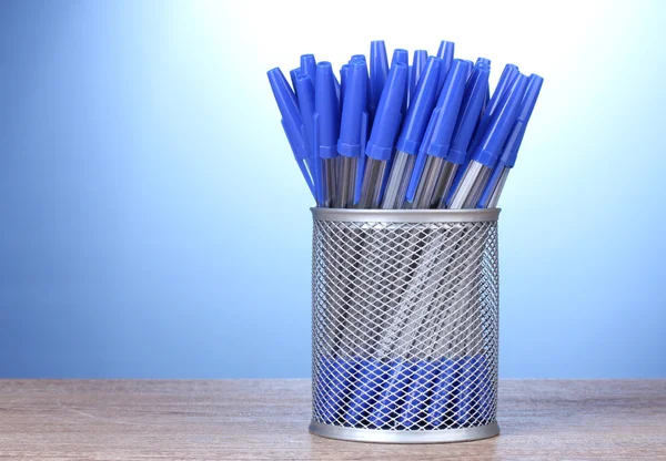 Blauwe pennen in metalen cup op houten tafel op blauwe achtergrond — Stockfoto
