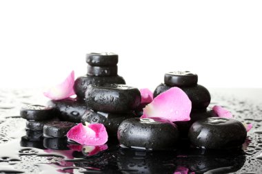 Spa stones with drops and rose petals on white background