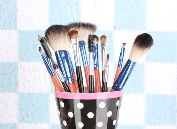 Pincéis de maquiagem em uma xícara preta de bolinhas no fundo colorido close-up — Fotografia de Stock