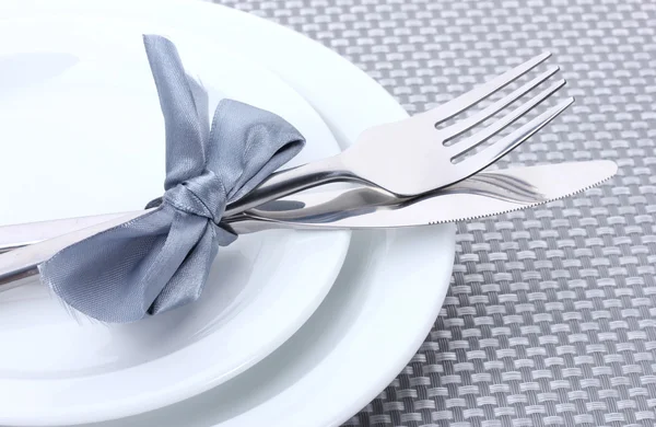 Bílé prázdné talíře s vidličkou a nožem svázané stuhou na šedé ubrus — Stock fotografie