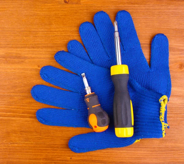 Schraubenzieher und Handschuhe auf Holzgrund — Stockfoto