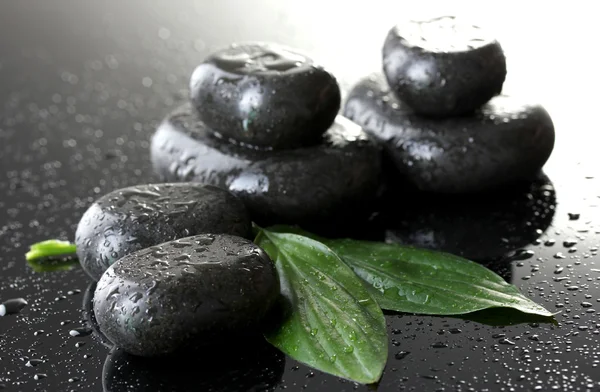 Spa stenen met druppels en groene bladeren op grijze achtergrond — Stockfoto