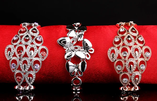 Três pulseiras elegantes no pano vermelho no fundo preto — Fotografia de Stock