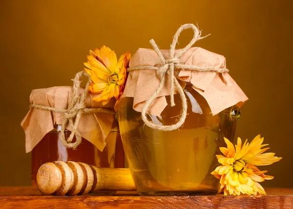 Twee potten van honing en houten drizzler op tafel op gele achtergrond — Stockfoto