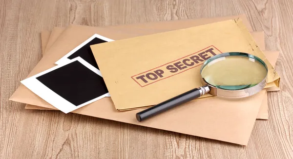 Envelopes com selo ultra-secreto com papéis fotográficos e lupa sobre fundo de madeira — Fotografia de Stock
