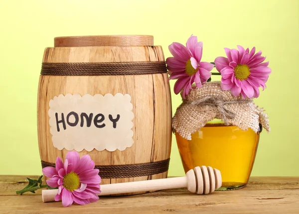 Сладкий мед в бочке и банке с капельницей на деревянном столе на зеленом фоне — стоковое фото