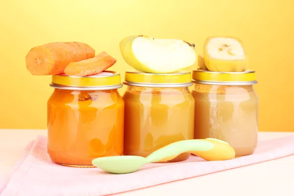 Jars of baby puree with spoon on napkin on yellow background — Stock Photo, Image
