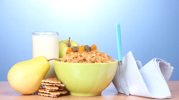 在绿色的碗和一杯牛奶在蓝色背景上的木桌上的美味玉米片 — 图库照片