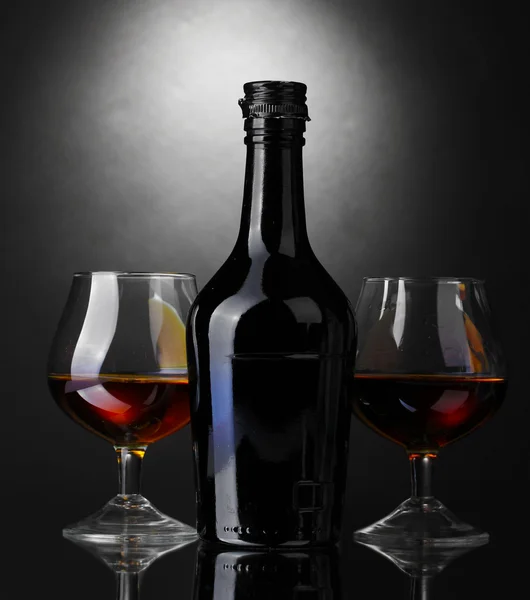 Brýle brandy a láhev na šedém pozadí — Stock fotografie