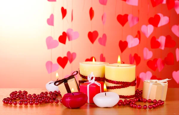 Mooie kaarsen met een romantische inrichting op een houten tafel op een rode achtergrond — Stockfoto