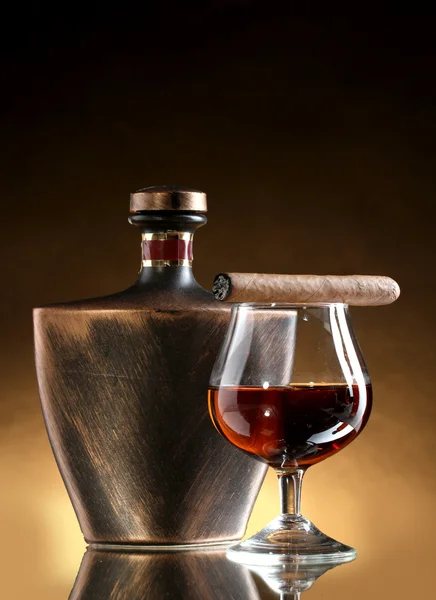 Botella y vaso de brandy y cigarro sobre fondo marrón — Foto de Stock