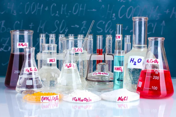 Reagenzgläser mit verschiedenen Säuren und anderen Chemikalien auf dem Hintergrund der Tafel — Stockfoto