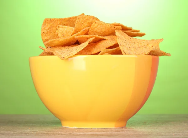 Tasty potato chips in yellow bowl on wooden table on green background — Stock Photo, Image