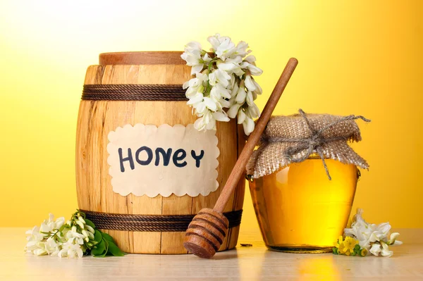 バレルとアカシアの花の黄色の背景に木製のテーブルの上の瓶に甘い蜂蜜 — ストック写真