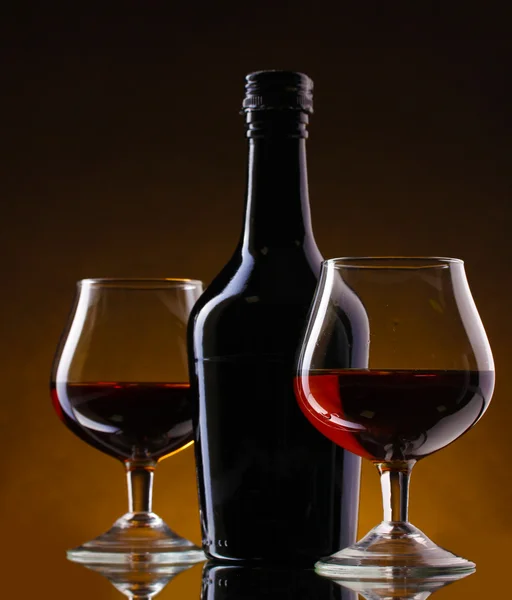 Gläser Schnaps und Flasche auf braunem Hintergrund — Stockfoto