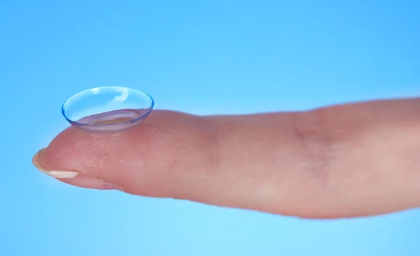 Contact lens on finger on blue background — Stock Photo, Image