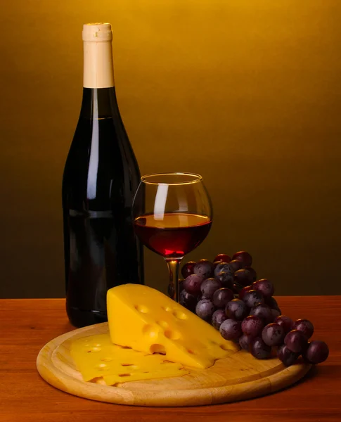 stock image Bottle of great wine with wineglass and cheese on wooden table on brown background