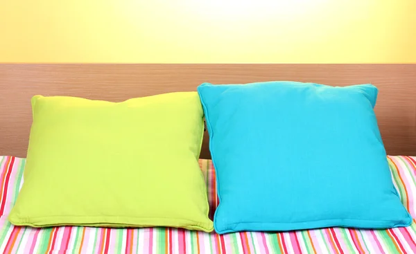 Helle Kissen auf dem Bett auf gelbem Hintergrund — Stockfoto