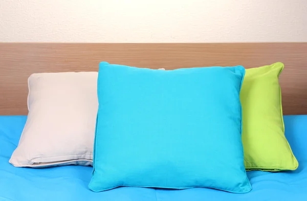 Cuscini luminosi sul letto su sfondo beige — Foto Stock