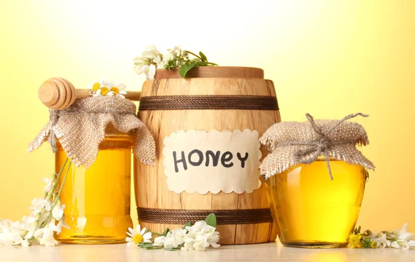 Édes méz hordó és üvegekbe a virágok akác fából készült asztal a sárga háttér — Stock Fotó