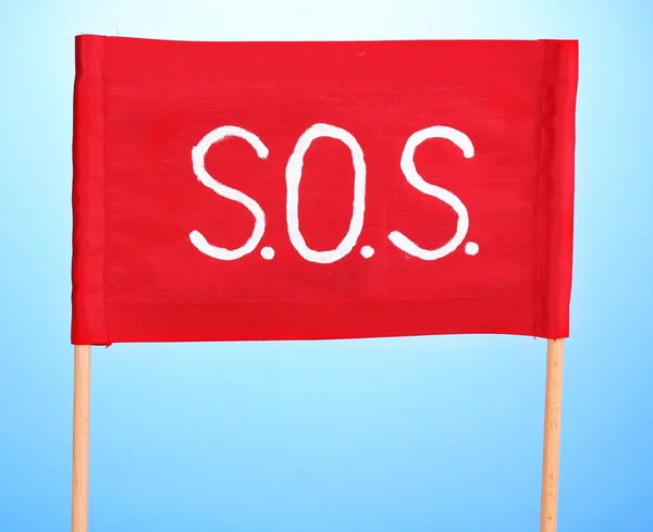 SOS sinal escrito em pano vermelho no fundo azul — Fotografia de Stock