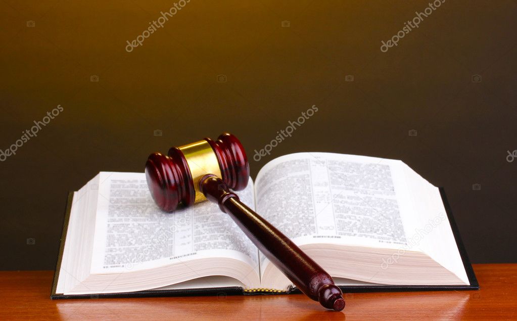 Judge's gavel and open book on wooden table on brown background